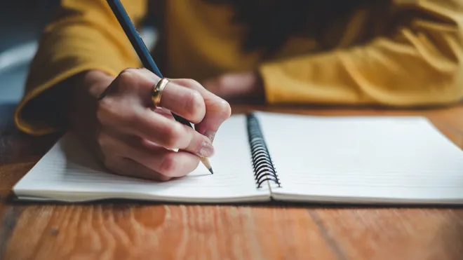 A person writing in a notebook with a pencil